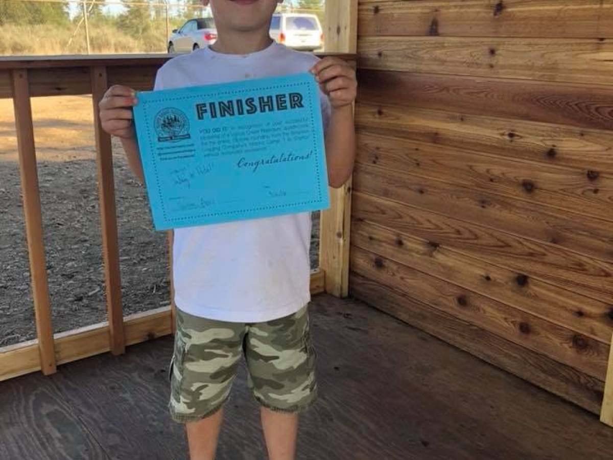 Child holding a blue finisher certificate on a wooden porch.