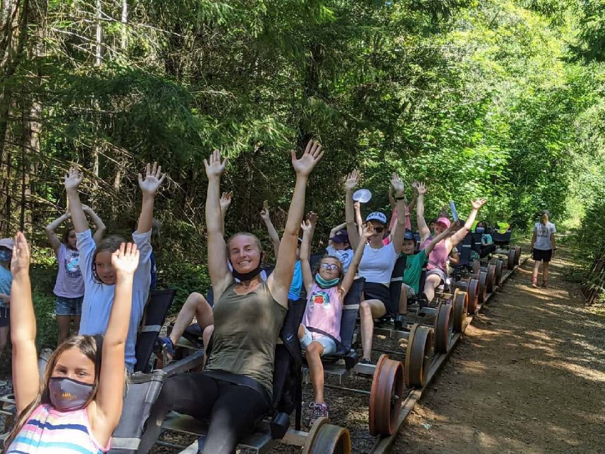 People on rail carts in the forest raising their arms and smiling.