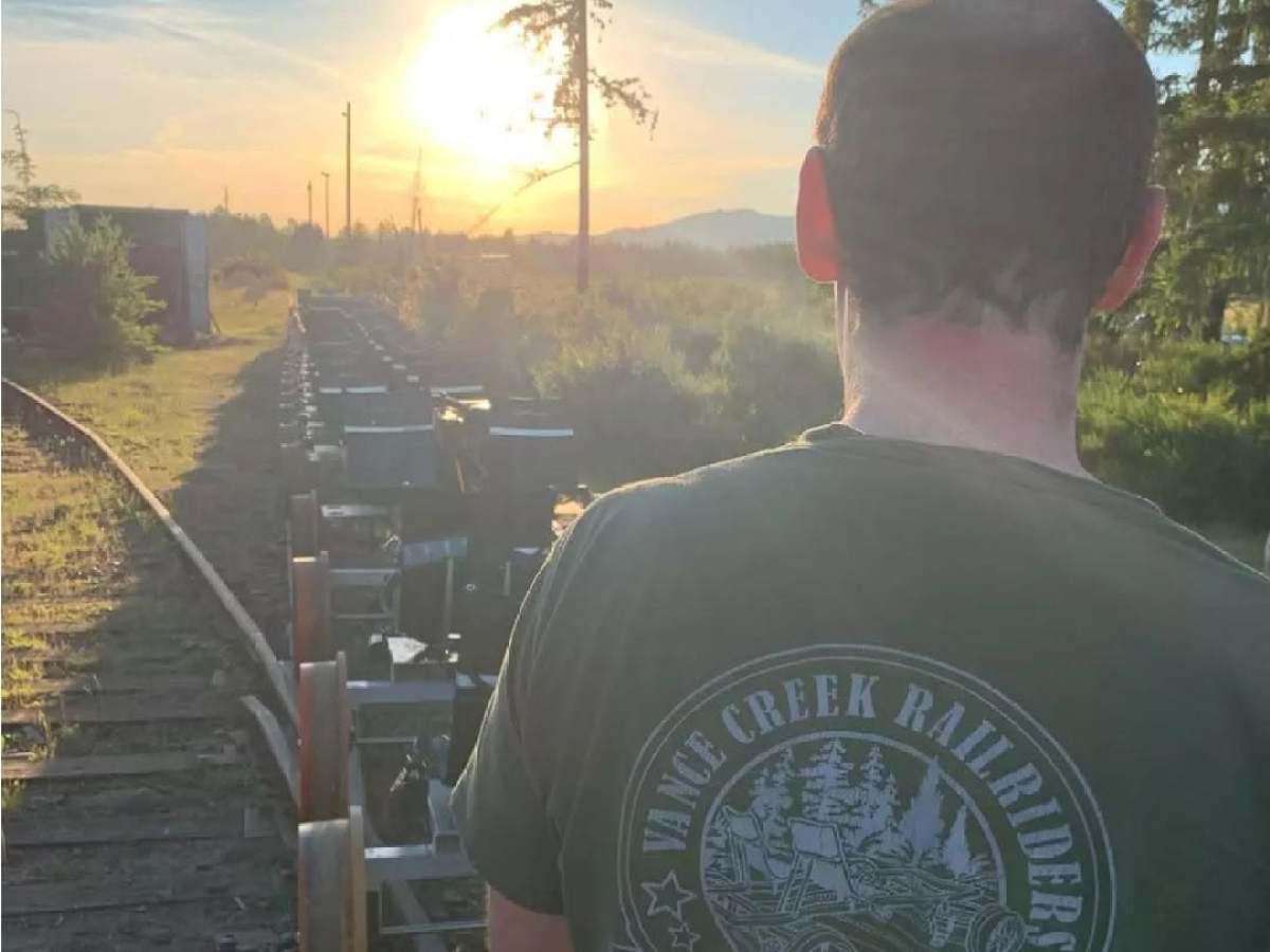 Man on rail bike at sunset, foliage and trees in background.