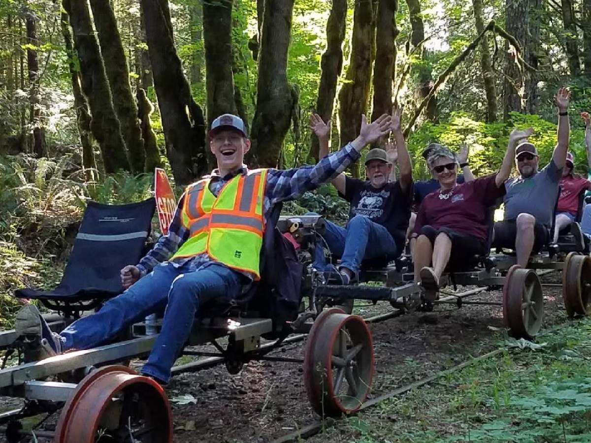 Group riding rail bikes through a forest, trees in background, people smiling and waving.