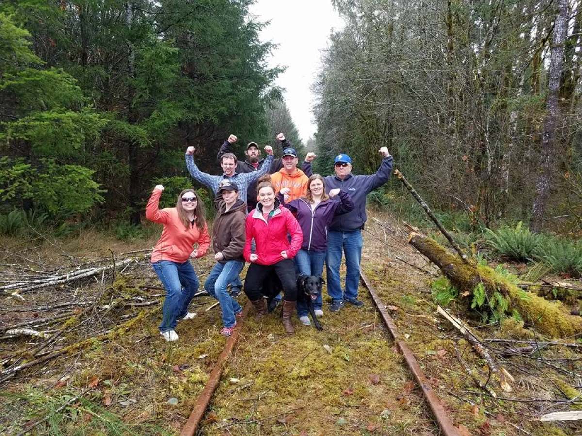 Group of people pose playfully on forest railway tracks.