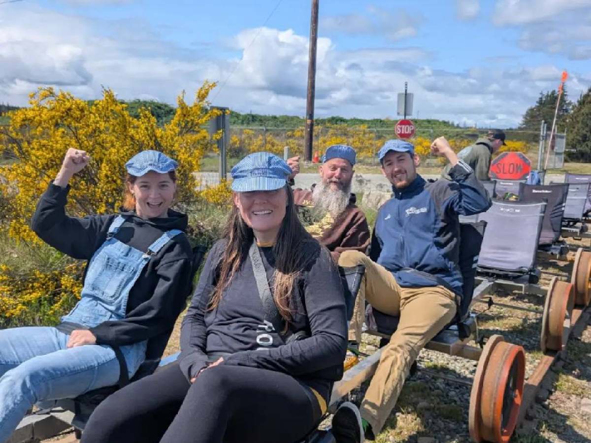 Four people in casual clothing ride a railbike on a sunny day.