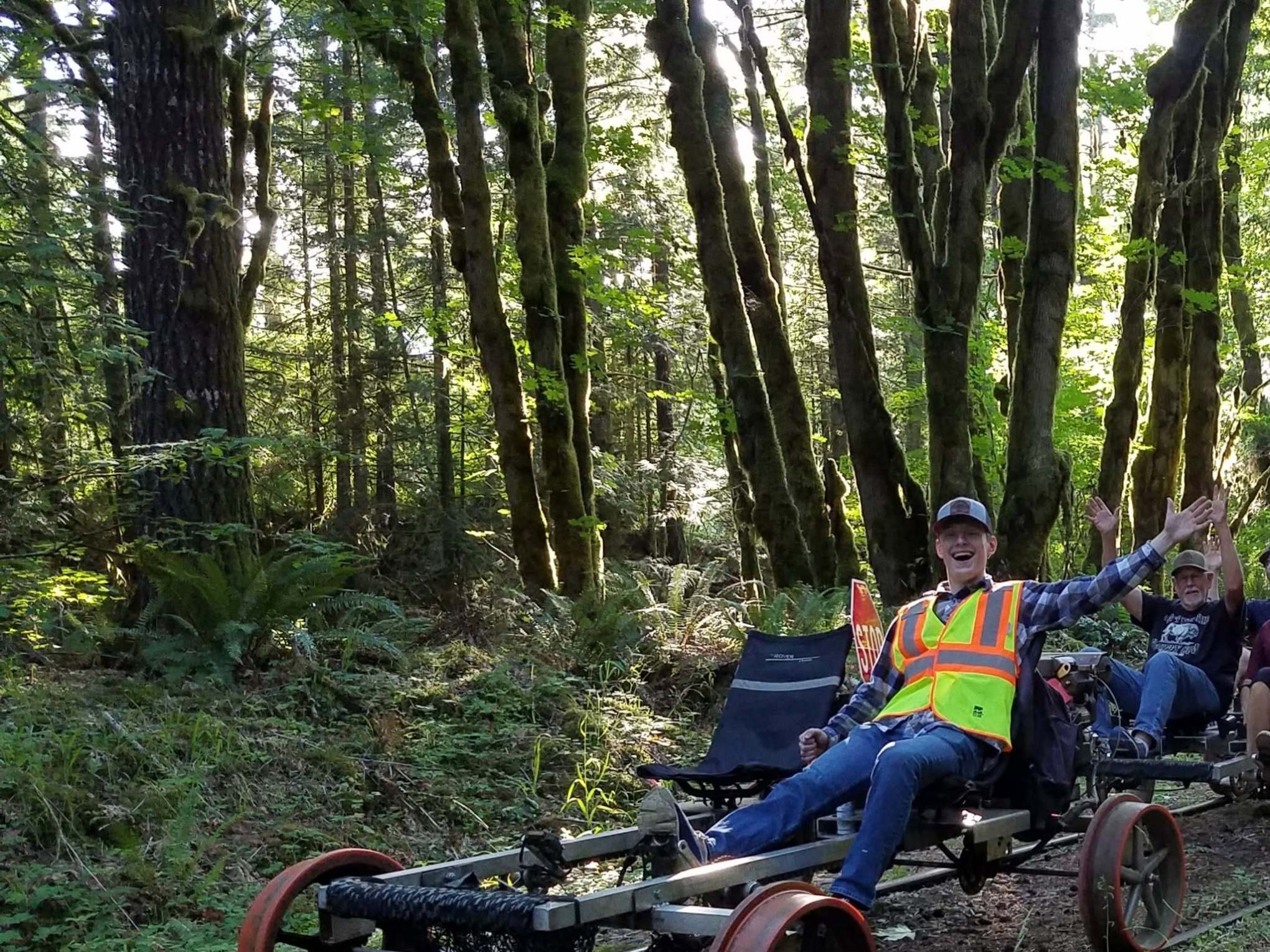 Person wearing a safety vest on a pedal car in a forested area.