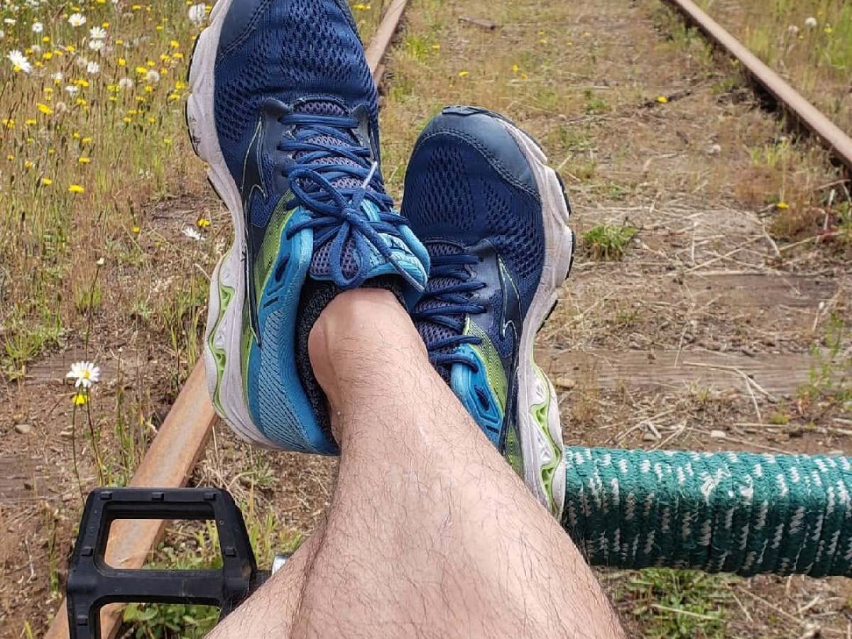 Person wearing blue sneakers relaxing on railroad track surrounded by wildflowers.