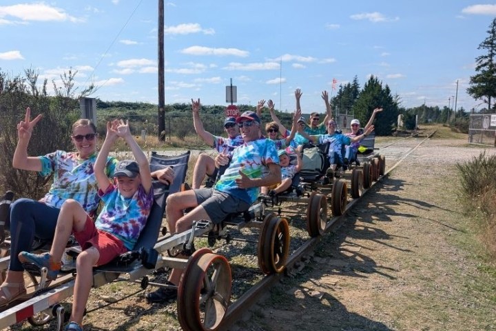 Group of people in tie-dye shirts riding pedal carts on railway tracks.
