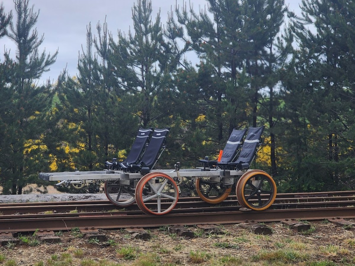 Two seats on a rail cart on train tracks in front of trees.
